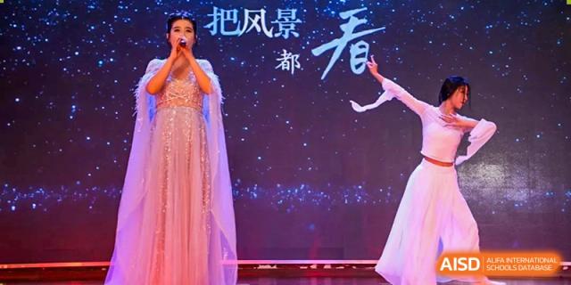 A female student in a sparkling pink gown singing on a dark stage with star-like lights in the background at Maple Leaf International School Wuhan.