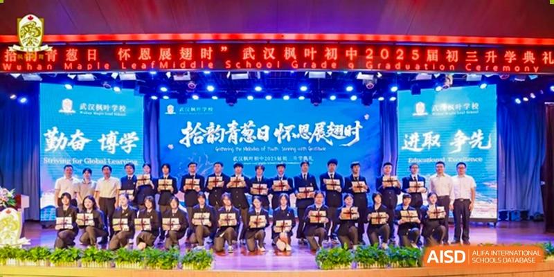 A large group of students in black uniforms posing together on a stage in front of a Chinese-language banner at Maple Leaf International School Wuhan.