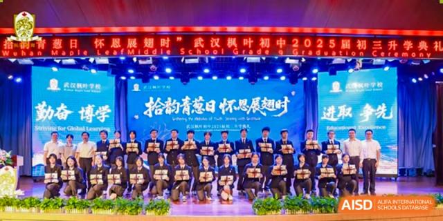 A large group of students in black uniforms posing together on a stage in front of a Chinese-language banner at Maple Leaf International School Wuhan.