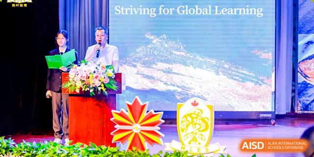 A male staff member speaking at a podium with a large screen displaying "Striving for Global Leadership" and the Maple Leaf logo at Maple Leaf International School Wuhan.