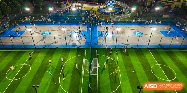 An aerial view of the brightly lit indoor sports complex with a soccer pitch and other courts at Maple Leaf International School Wuhan.