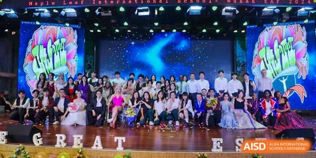 A large group of students and staff members posing together for a group photo on a dark, illuminated stage at Maple Leaf International School Wuhan.