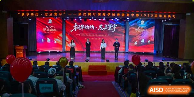 Students and staff standing on a stage in front of a large, red screen with Chinese text during a formal school ceremony at Maple Leaf International School Wuhan.