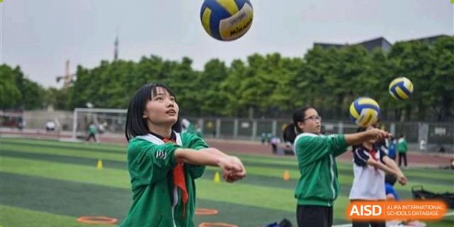 A female student in a green shirt attempting to bump a volleyball during an outdoor sports activity at Maple Leaf International School Wuhan.