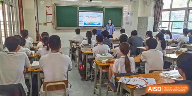 A teacher in a mask instructing a class of students who are seated at desks facing a presentation screen at Oxstand International School, Shenzhen.