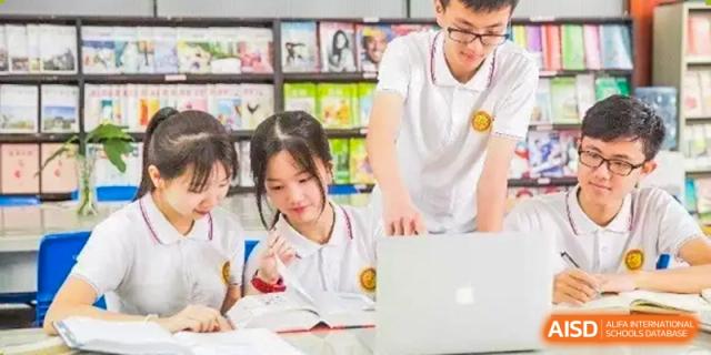 A male teacher assisting a female student who is working on a laptop in the school library or study area at Oxstand International School, Shenzhen.