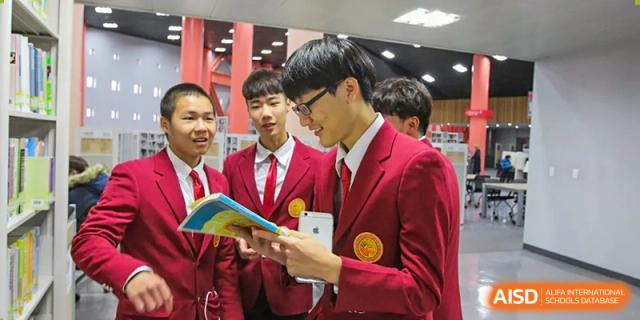 Two male students in red school blazers reviewing materials together while standing with classmates at Oxstand International School, Shenzhen.