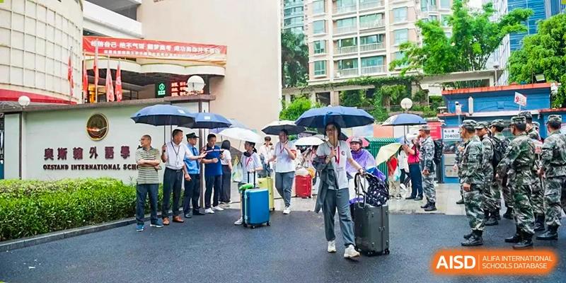 Students and parents standing outside with luggage and umbrellas, suggesting arrival or departure at Oxstand International School, Shenzhen.