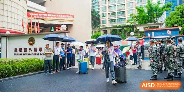 Students and parents standing outside with luggage and umbrellas, suggesting arrival or departure at Oxstand International School, Shenzhen.