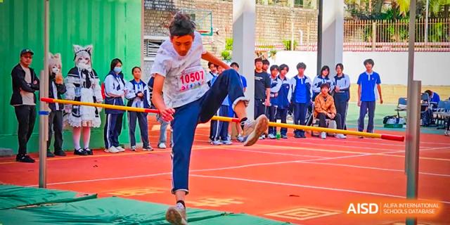 A male student in a white t-shirt performing a kick during an outdoor martial arts or physical education demonstration at Oxstand International School, Shenzhen.
