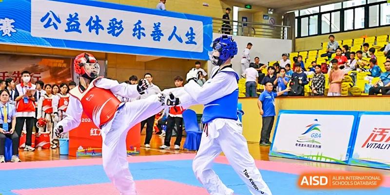 Two students in blue and white Taekwondo gear sparring during a demonstration in front of a crowd at Oxstand International School, Shenzhen.