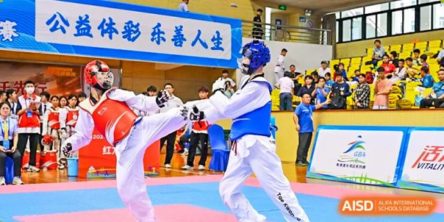 Two students in blue and white Taekwondo gear sparring during a demonstration in front of a crowd at Oxstand International School, Shenzhen.