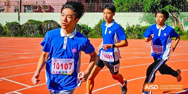 Two male students in blue and white uniforms running on a red track during a sports day event, with one wearing a bib number 10107 at Oxstand International School, Shenzhen.