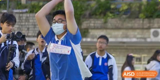 A male student in a blue sports jersey and a mask raising his arms in celebration or competition at Oxstand International School, Shenzhen.