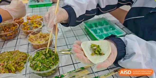 A student's hands, wearing clear gloves, carefully placing green filling onto a dumpling wrapper during a cooking class at Oxstand International School, Shenzhen.