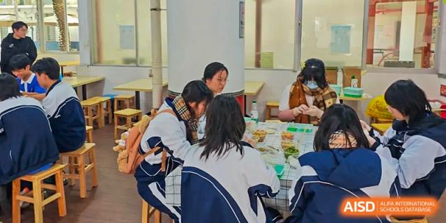 A group of students in uniform gathered around a table and actively working on a cooking or food preparation activity at Oxstand International School, Shenzhen.