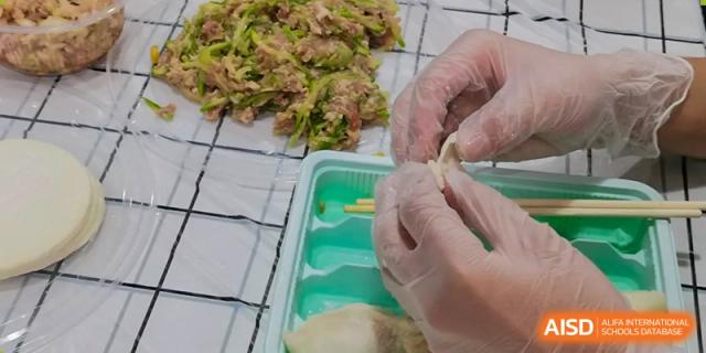 A student's hands, wearing gloves, delicately pinching the edges of a dumpling closed over the filling at Oxstand International School, Shenzhen.