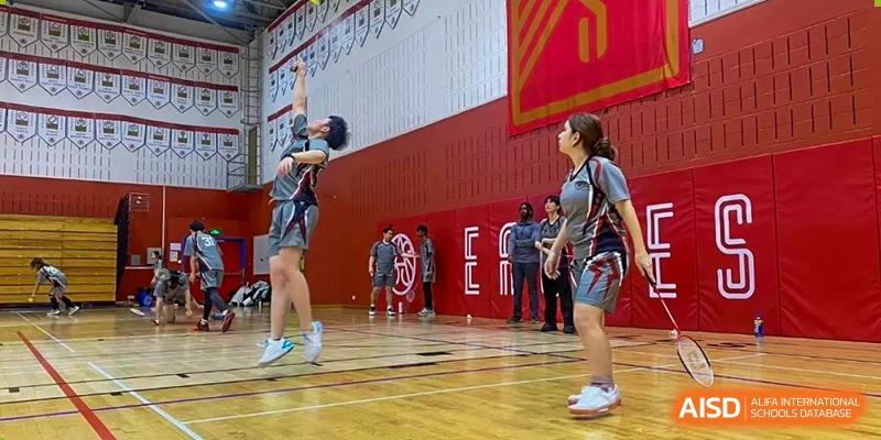 A Shanghai Livingston American School student shooting a basketball in an indoor gym, with another player defending.