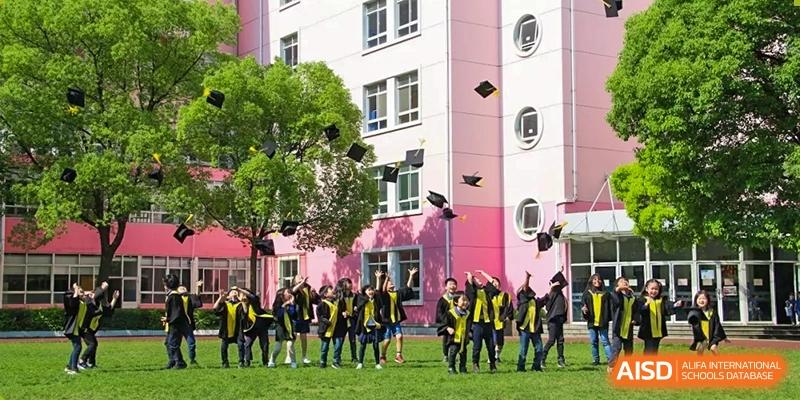 Shanghai Livingston American School students dressed in uniform posing for a photo in front of a school building with pink walls.