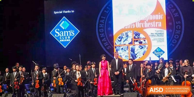 Shanghai Livingston American School students performing as an orchestra on a stage with a red-dressed conductor/performer in the foreground.