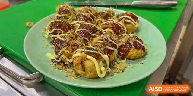 A plate of Takoyaki (octopus balls) with sauce and mayonnaise, representing the diverse culinary offerings at Shanghai Livingston American School.