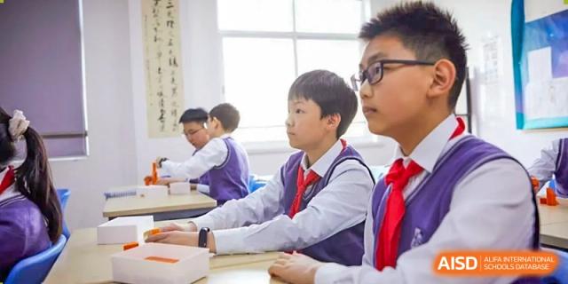 Students in school uniforms sitting at desks in a classroom, with one student looking to the right, at Shanghai United International School (SUIS-Jiaoke) Jiaoke Campus.