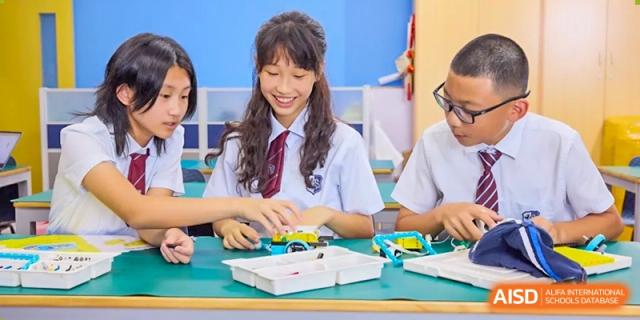 A female student in uniform smiling while working on a hands-on project or activity with small components at Shanghai United International School (SUIS-Jiaoke) Jiaoke Campus.