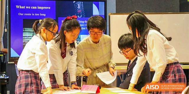 A teacher or mentor in glasses reviewing documents with two students in an academic or club setting at Shanghai United International School (SUIS-Jiaoke) Jiaoke Campus.
