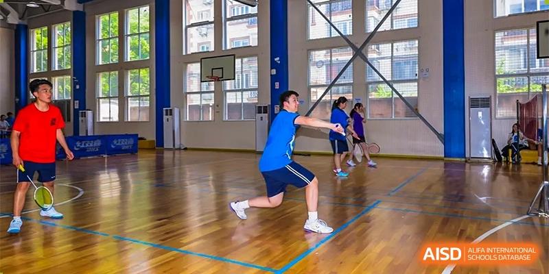 A male student running forward to hit a shuttlecock during an indoor badminton or sports practice in the school gymnasium at Shanghai United International School (SUIS-Jiaoke) Jiaoke Campus.