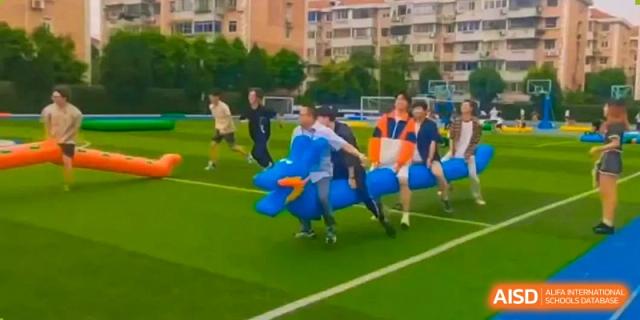 Students participating in a fun outdoor relay race or game involving a large inflatable blue horse on the sports field at Shanghai United International School (SUIS-Jiaoke) Jiaoke Campus.