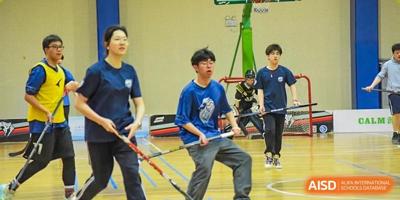 A Shanghai United International School (SUIS-Jiaoke) Jiaoke Campus student participating in an indoor floor or field hockey-like sport, holding a stick on a gymnasium court.