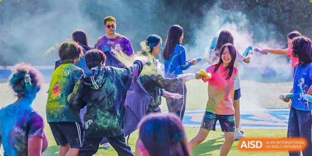 Shanghai United International School (SUIS-Jiaoke) Jiaoke Campus students celebrating at a colorful outdoor event, being playfully covered in powdered paint (Holi festival or similar color celebration).