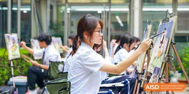 Close-up of a student in a white shirt and glasses focused on an activity, possibly a performance or competition, at Shanghai United International School (SUIS-Jiaoke) Jiaoke Campus.