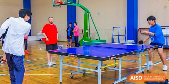 A table tennis table set up in a gymnasium, with students and spectators in the background at Shanghai United International School (SUIS-Jiaoke) Jiaoke Campus.