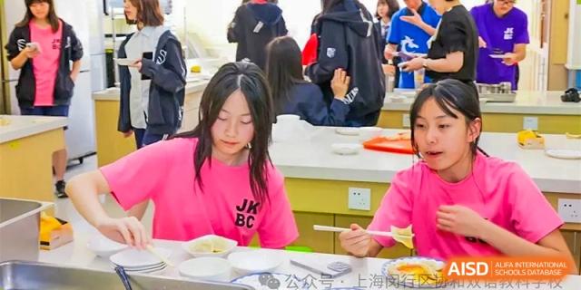 A female student in a bright pink shirt with "JKBC" on it, eating a meal in the cafeteria or dining area at Shanghai United International School (SUIS-Jiaoke) Jiaoke Campus.