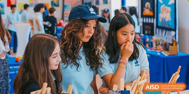 Two female high school students in school polo shirts looking intently at their work or a project outdoors at Western International School of Shanghai.
