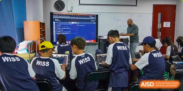 Two male students focused on a computer screen displaying code or a technical program in a classroom at Western International School of Shanghai.