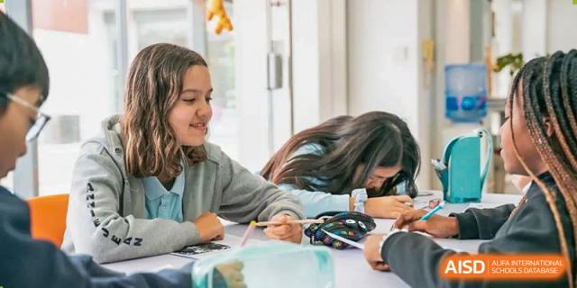 A small group of students collaborating on a tabletop project in a bright, modern classroom at Western International School of Shanghai.