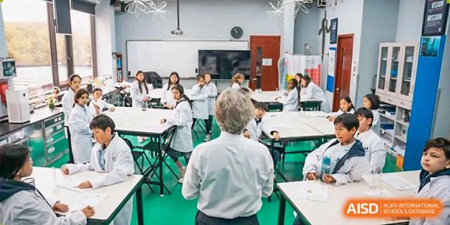 An overhead shot of an older teacher talking to a student in a large, bright classroom or lecture hall at Western International School of Shanghai.