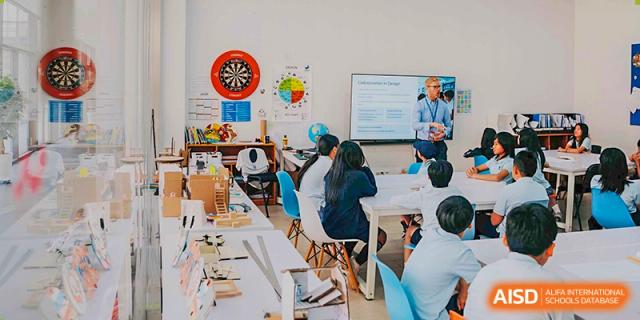 A classroom of students working together on a project, with a teacher assisting, in a brightly lit learning space at Western International School of Shanghai.