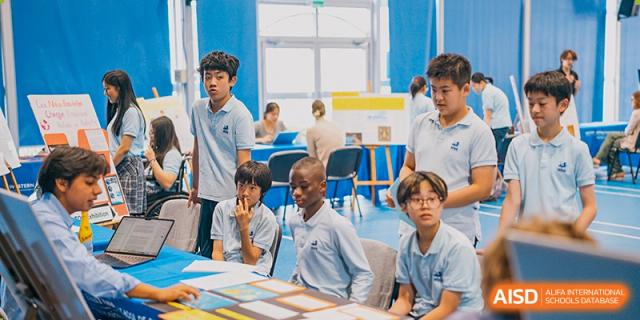 A diverse group of middle or high school students seated at a table, focused on a project display at a student exhibition at Western International School of Shanghai.
