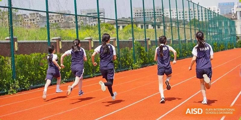 Students in uniform running on the outdoor red track during a physical education or sports class at Western International School of Shanghai.
