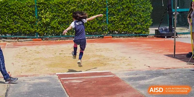 A student mid-air while performing a long jump on the red track and sandpit at Western International School of Shanghai.