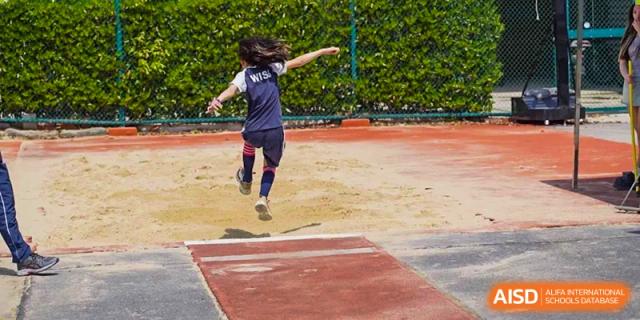 A student mid-air while performing a long jump on the red track and sandpit at Western International School of Shanghai.