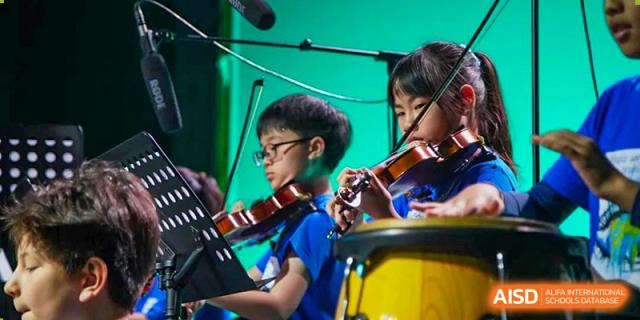 Young students playing musical instruments, including a violin, on a stage during a performance at Western International School of Shanghai.