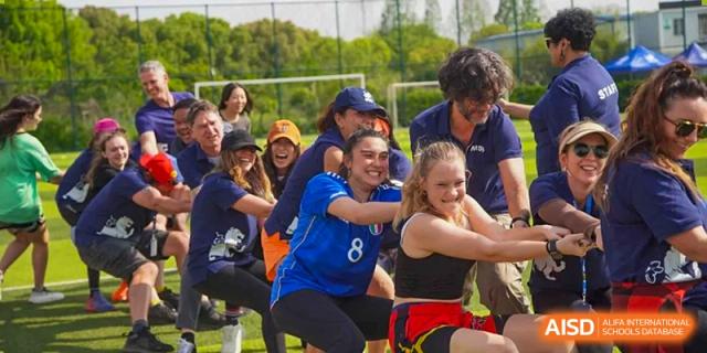 A team of students and adults participating in a fun outdoor tug-of-war competition during a field day event at Western International School of Shanghai.