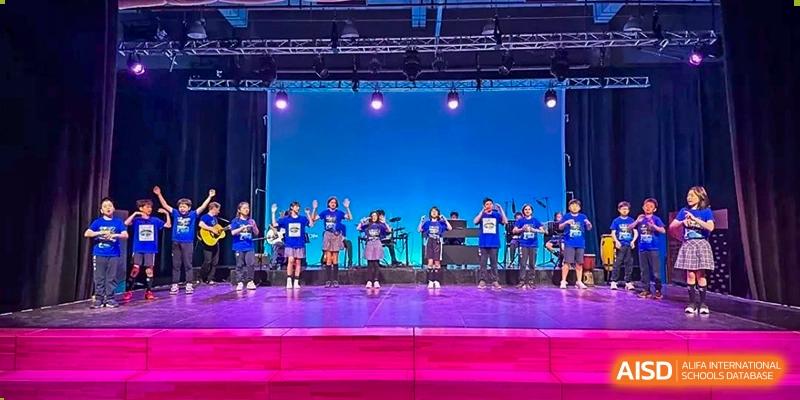 A group of students performing a band or dance routine on a brightly lit stage outdoors during a school festival at Western International School of Shanghai.