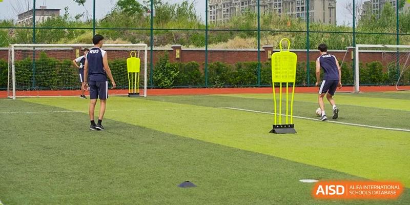 An outdoor artificial turf field for sports and physical education, bordered by a brick wall and practice cones, at Western International School of Shanghai.