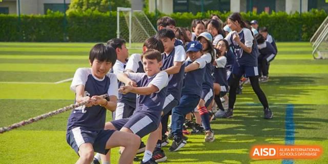 A group of middle or high school students participating in a tug-of-war game on a grassy field at Western International School of Shanghai.