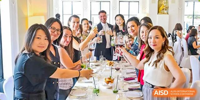 A group of happy adults, including teachers and parents, toasting with wine at a formal dinner or school function at Western International School of Shanghai.